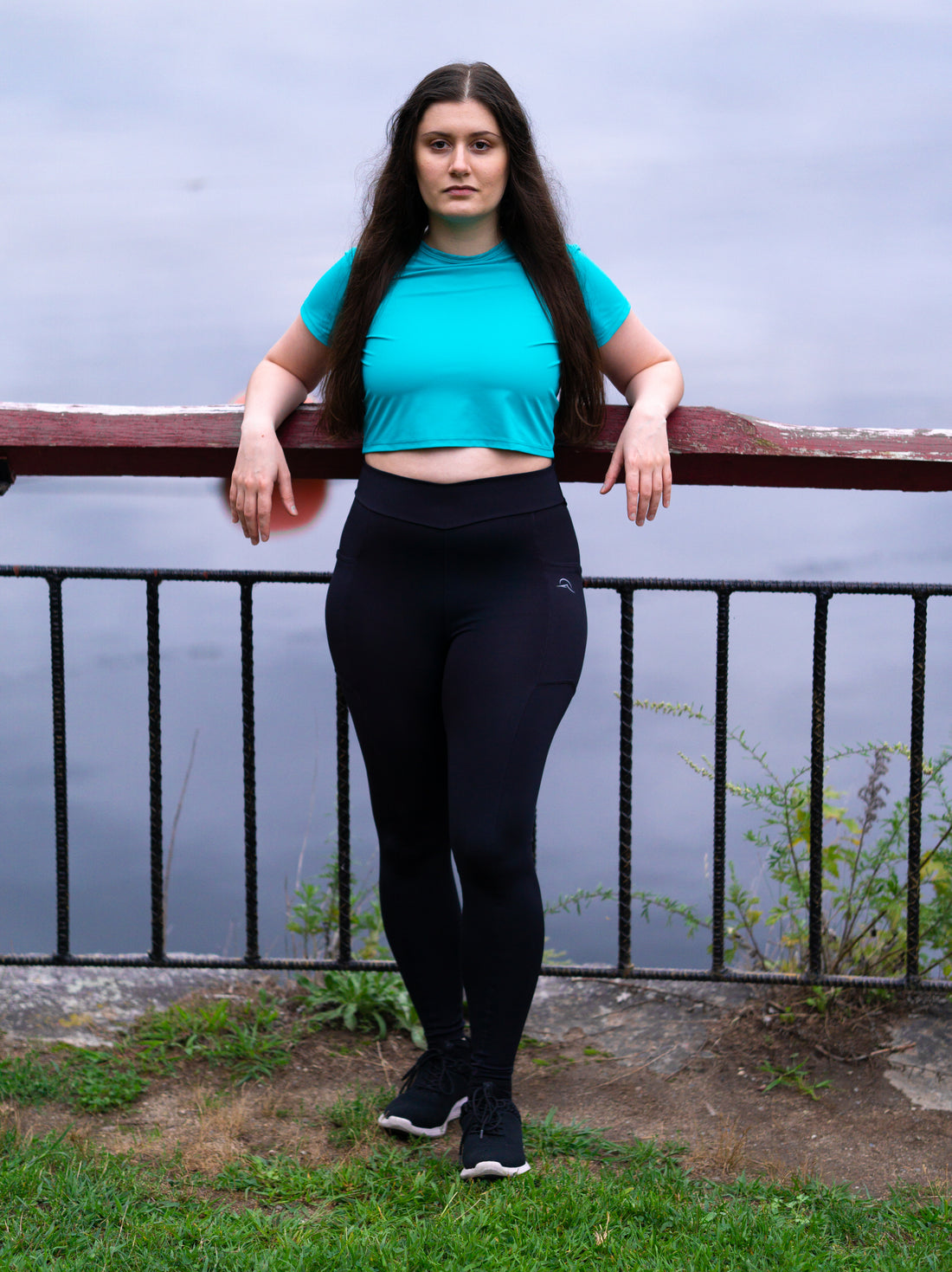 Woman in leggings with pockets and crop top leaning against fence