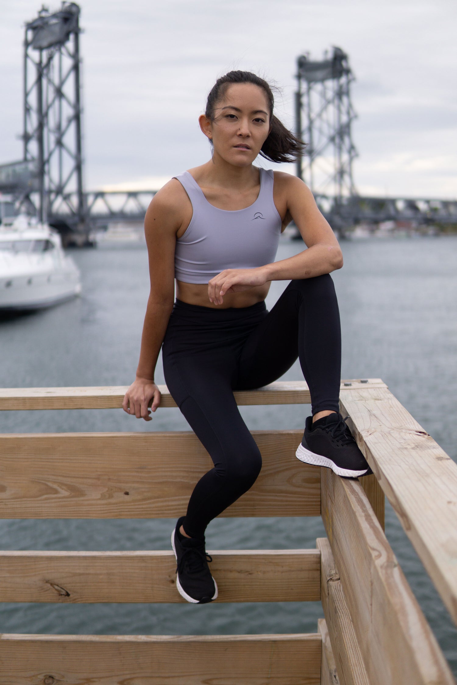 pony-tailed woman sitting on wooden deck wearing sports bra and leggings