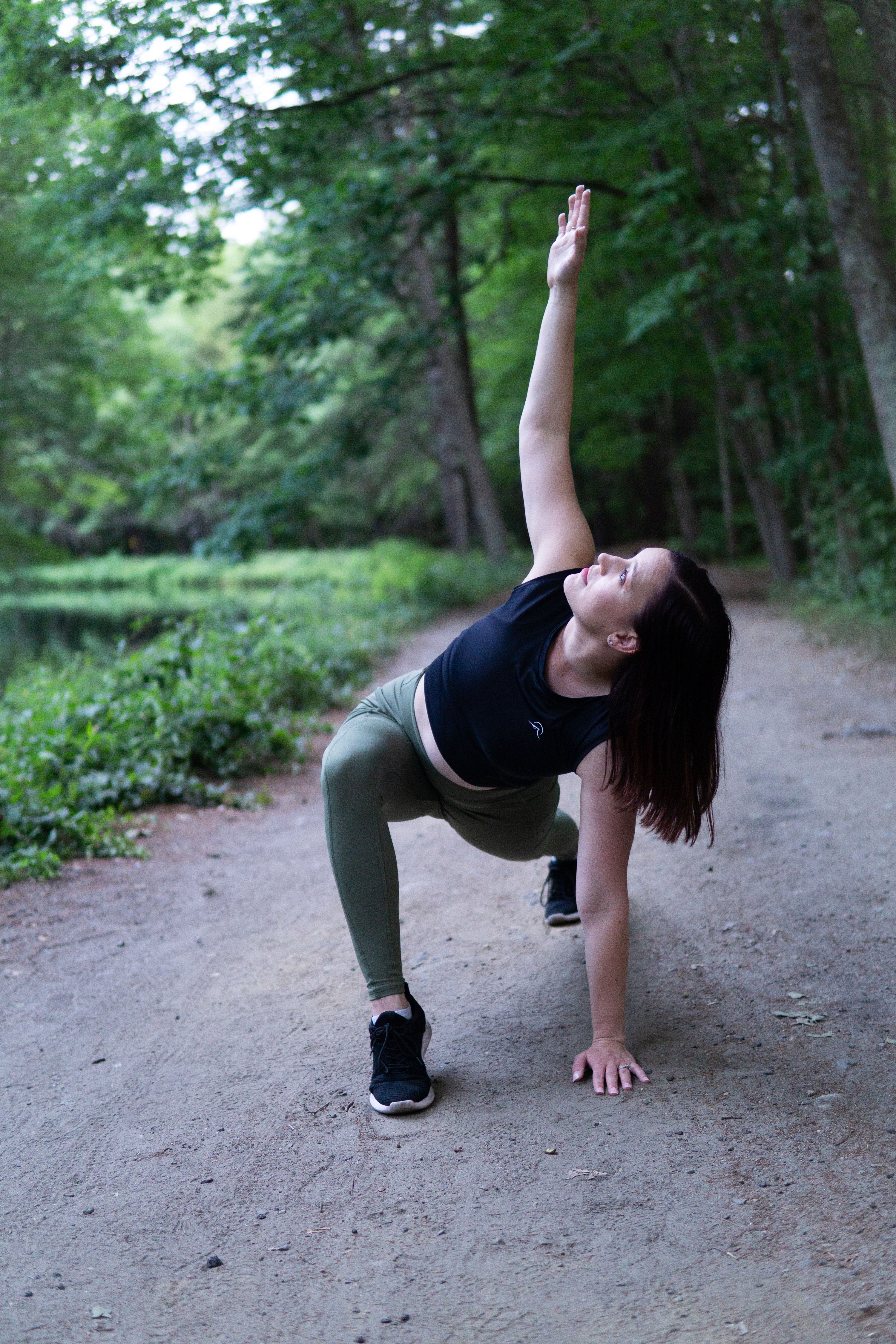 woman wearing sustainable black crop-top and olive leggings stretching on a dirt track